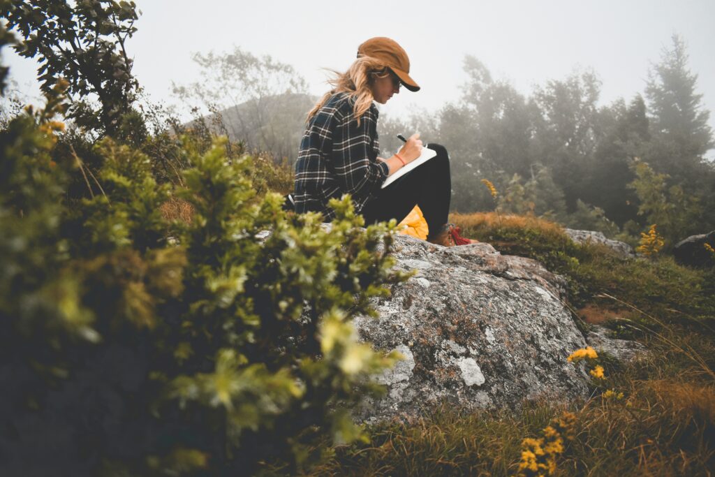 A woman sitting on a boulder journaling on how to set goals with intention.