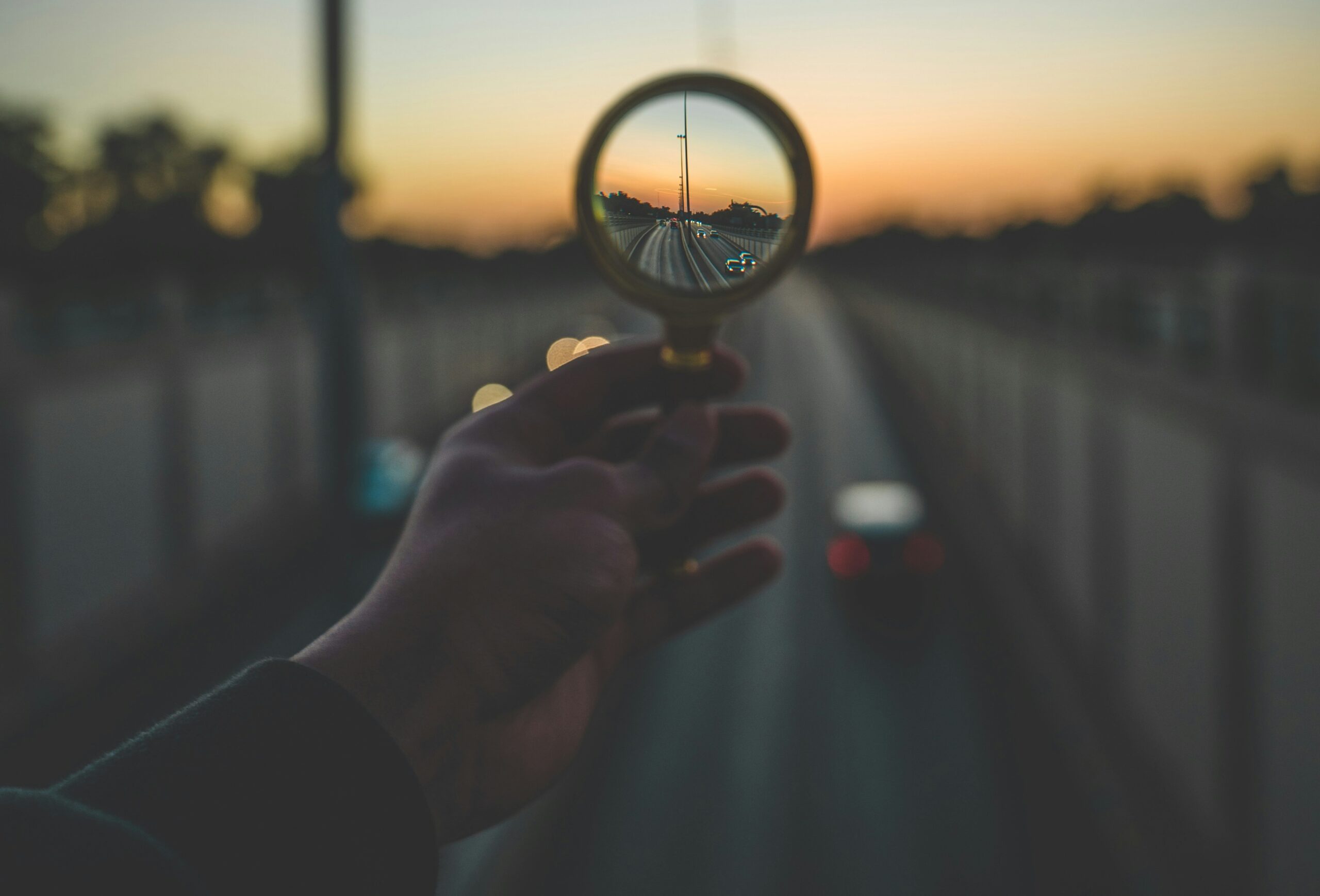 Close up of a person holding a magnifying glass looking toward the horizon, representative of goal setting with intention.