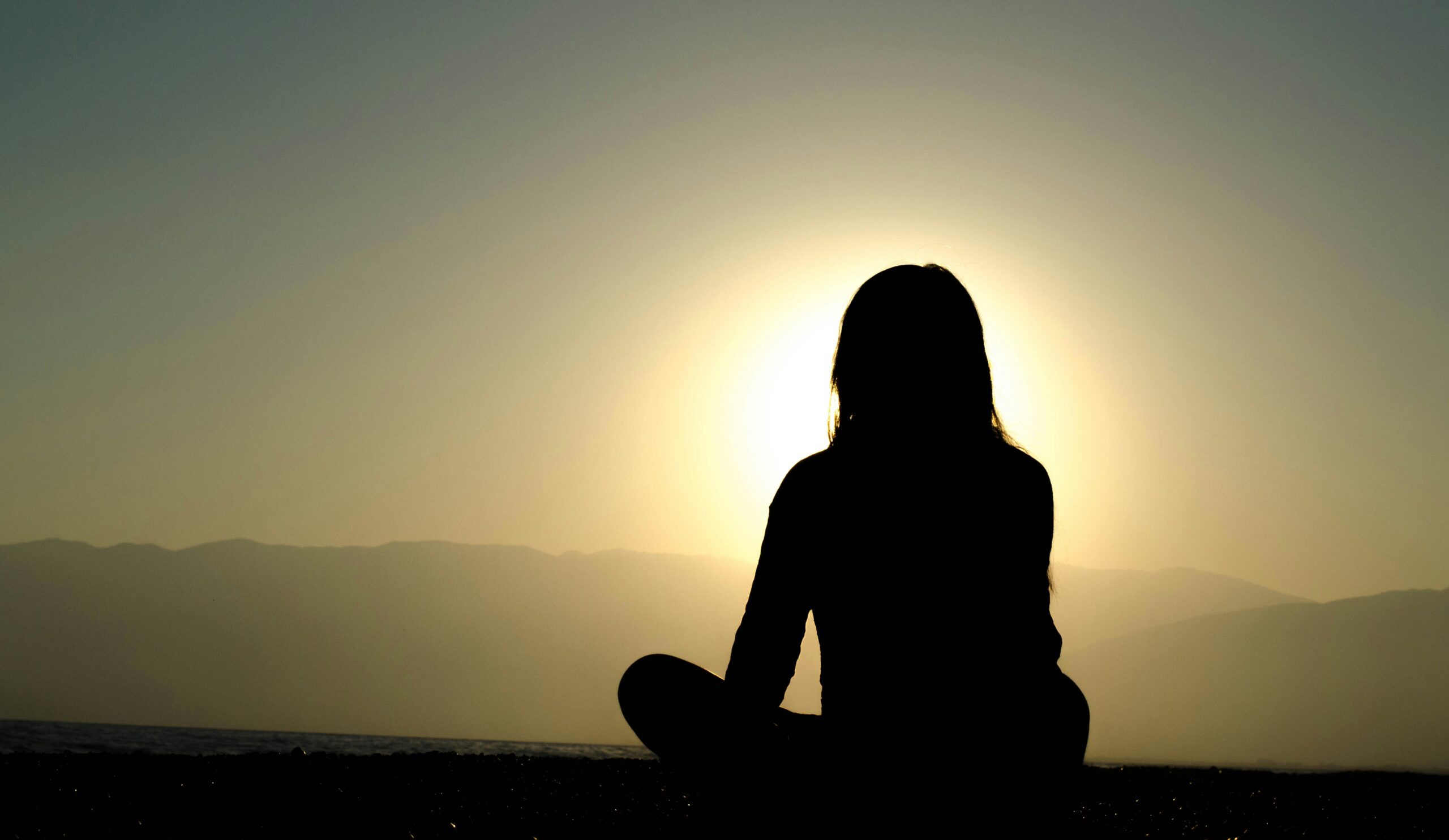 Silhouette of person sitting on a mountain ridge thinking about the benefits of meditation.