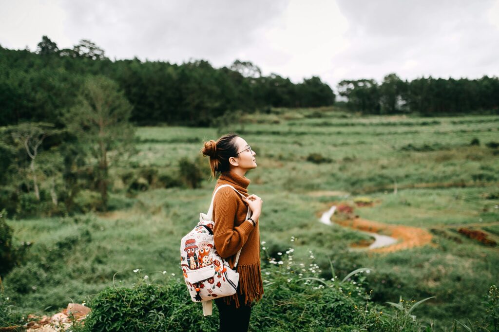 Woman standing in green field with her eyes closed, thinking about the benefits of meditation.
