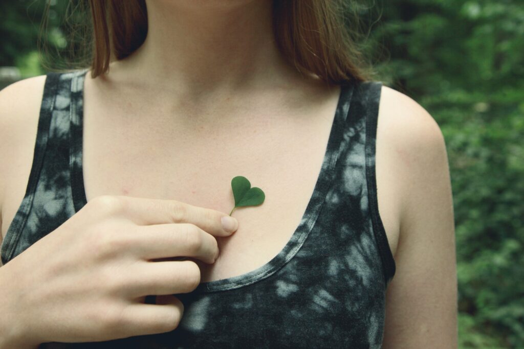 Close up of a person holding a heart shaped leaf on their chest and thinking about pendulation and somatic therapy.