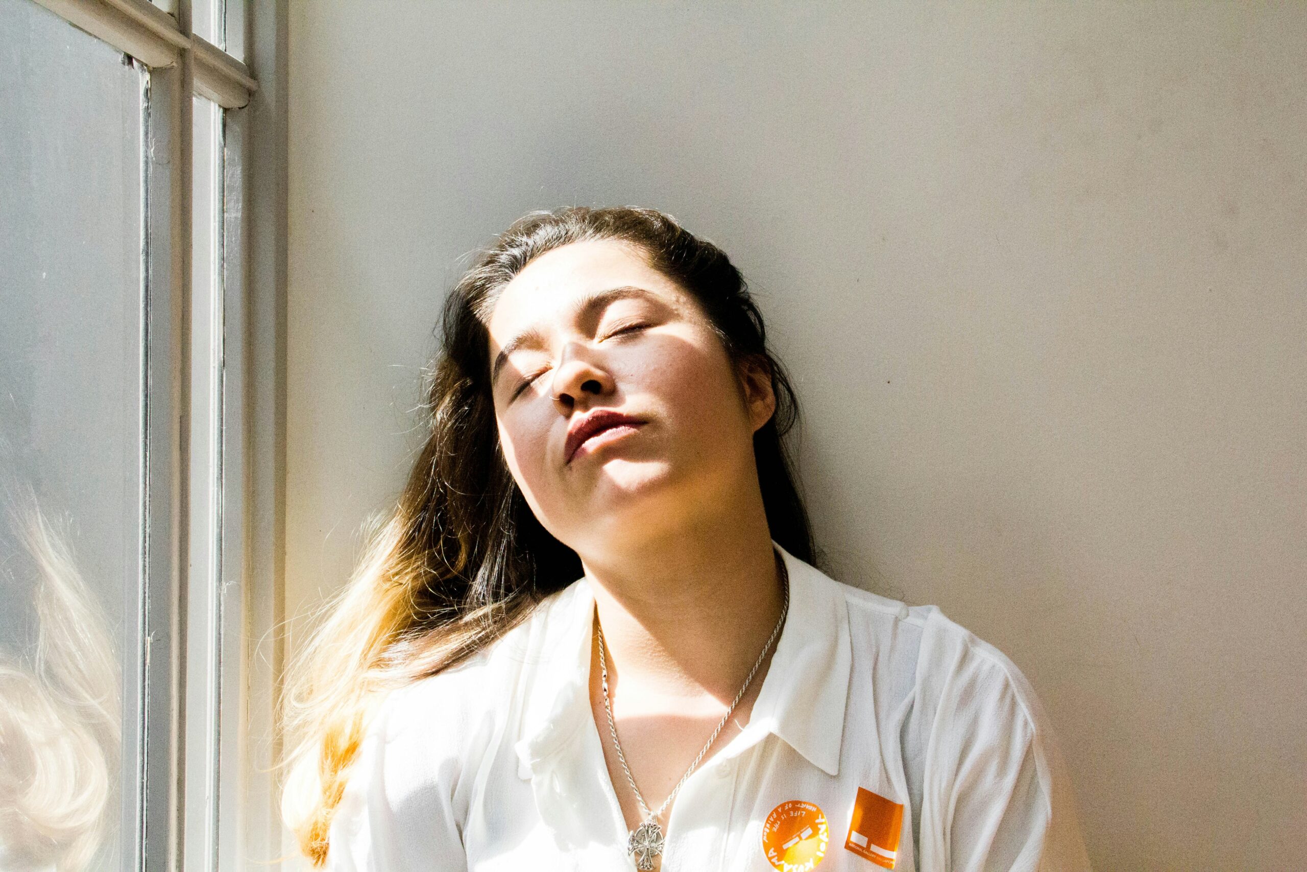 Woman leaning against a wall by a window with her eyes closed after using her mental energy.