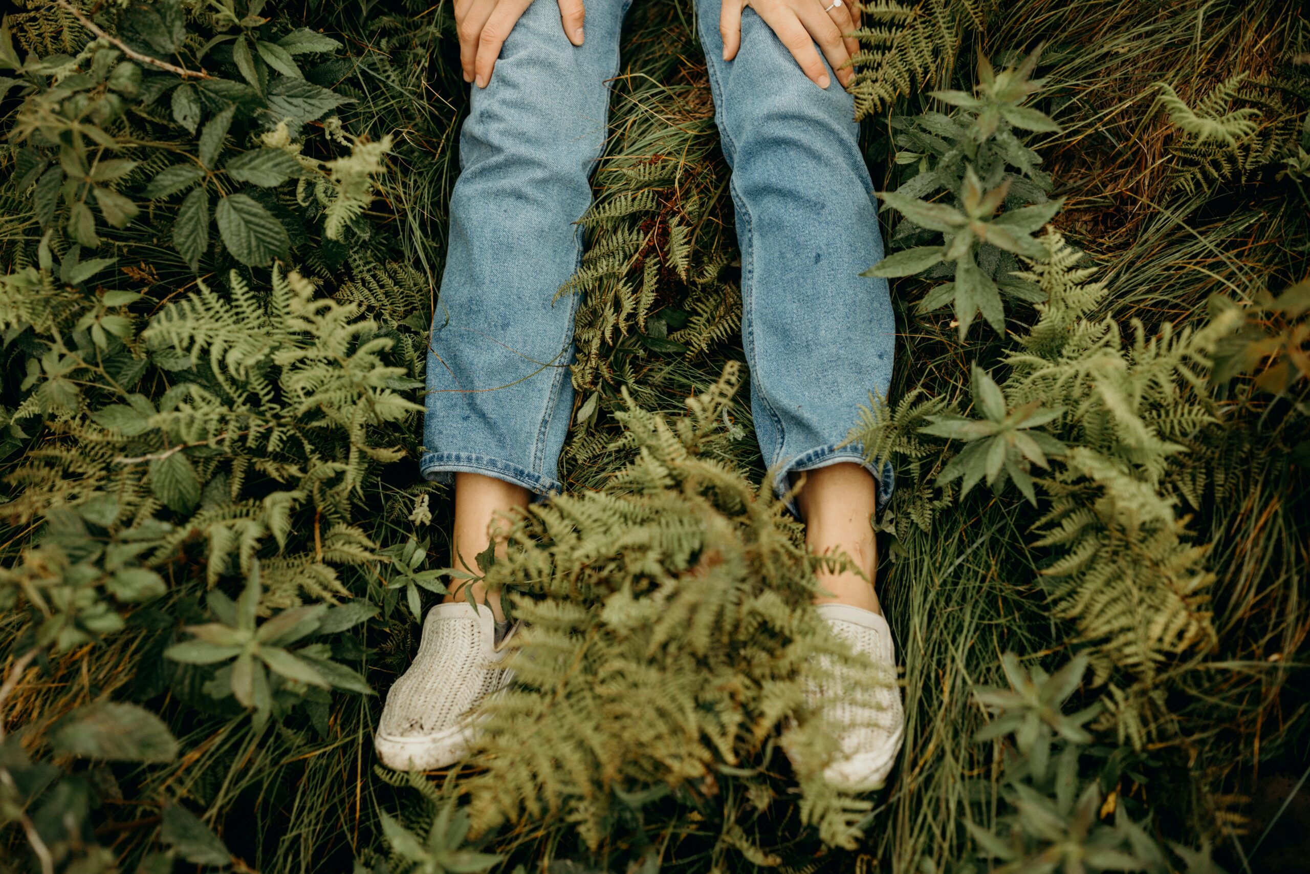 A close up of legs and feet laying in a bed of fern in Bend, Oregon, representing body awareness.