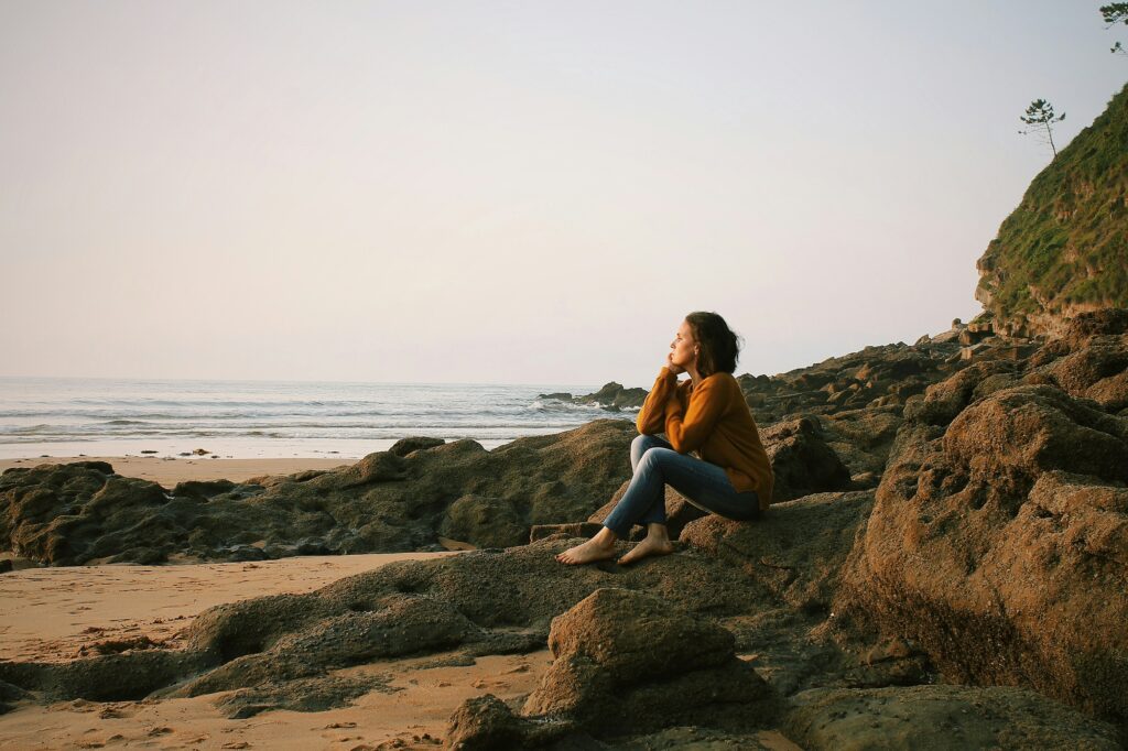 Woman sitting on a beach, looking out at the water, after practicing body awareness at therapy in Bend Oregon.